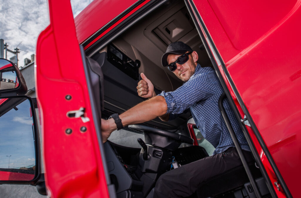 A happy semi-truck driver gives a thumbs up as he gets into his vehicle to show his gratitude after having the semi-truck serviced.