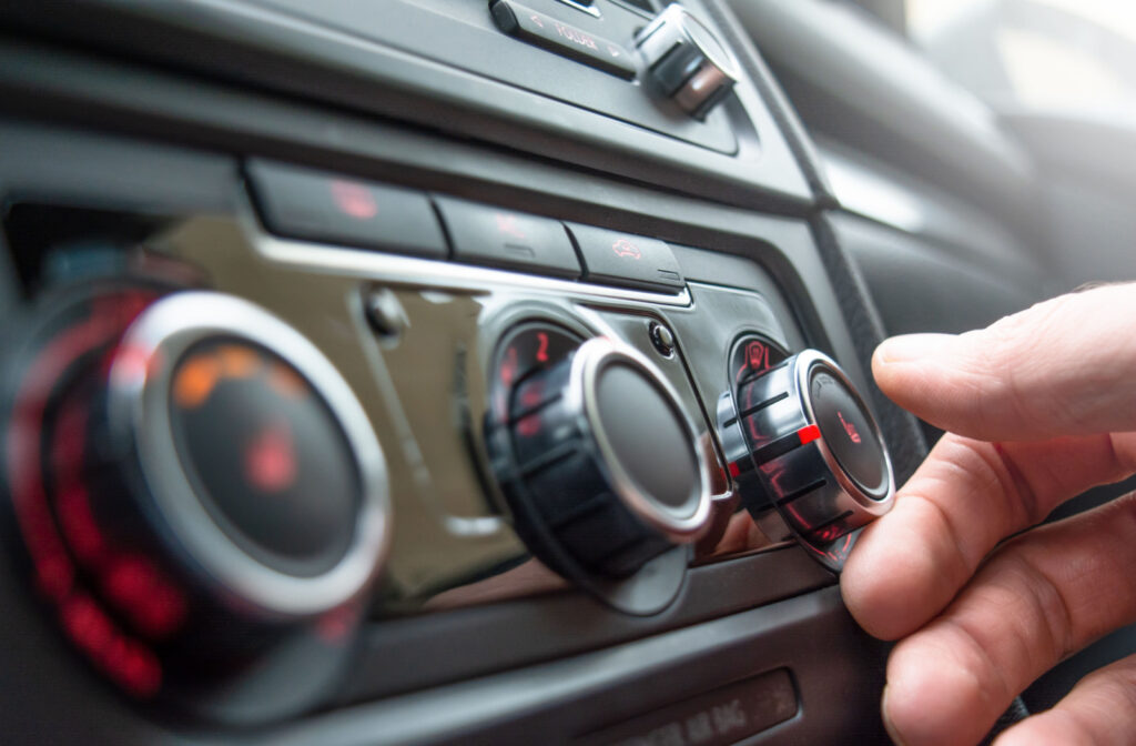 A close-up of a car heater settings with a man's hand trying to reach for the knob