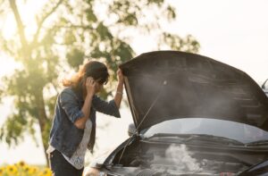 A woman looking at her car engine with an open front hood as smoke comes out of it
