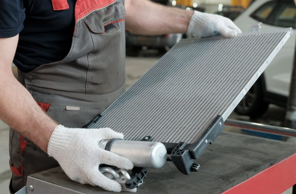 a mechanic holding an aluminum radiator with both hands