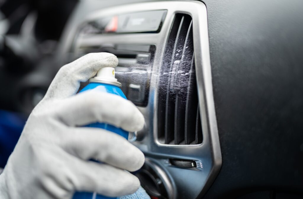 A close-up image of someone spraying a cleaning solution into a car's vents.