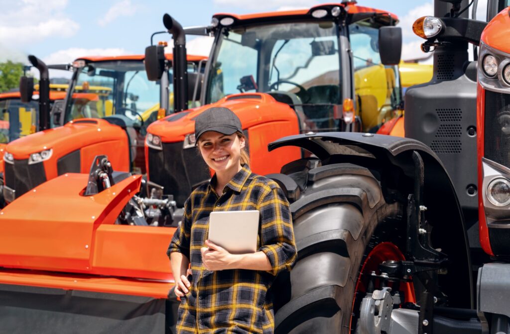 A young adult smiling and holding a tablet in front of a cleaned and repaired row of Kubota tractors.
