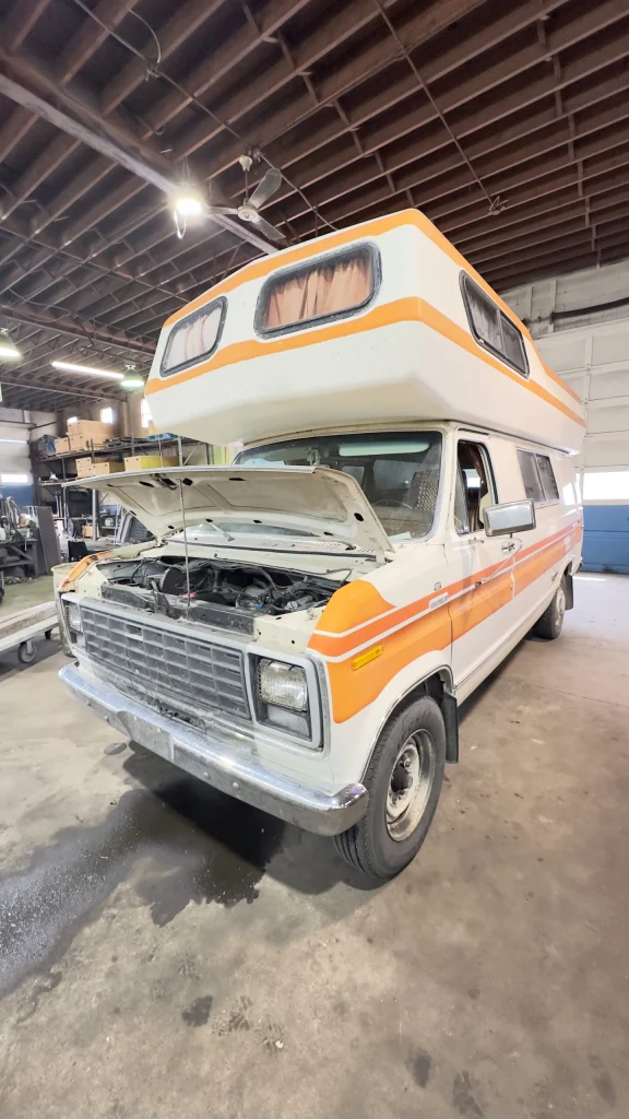 A retro camper van with its hood raised sits in a garage