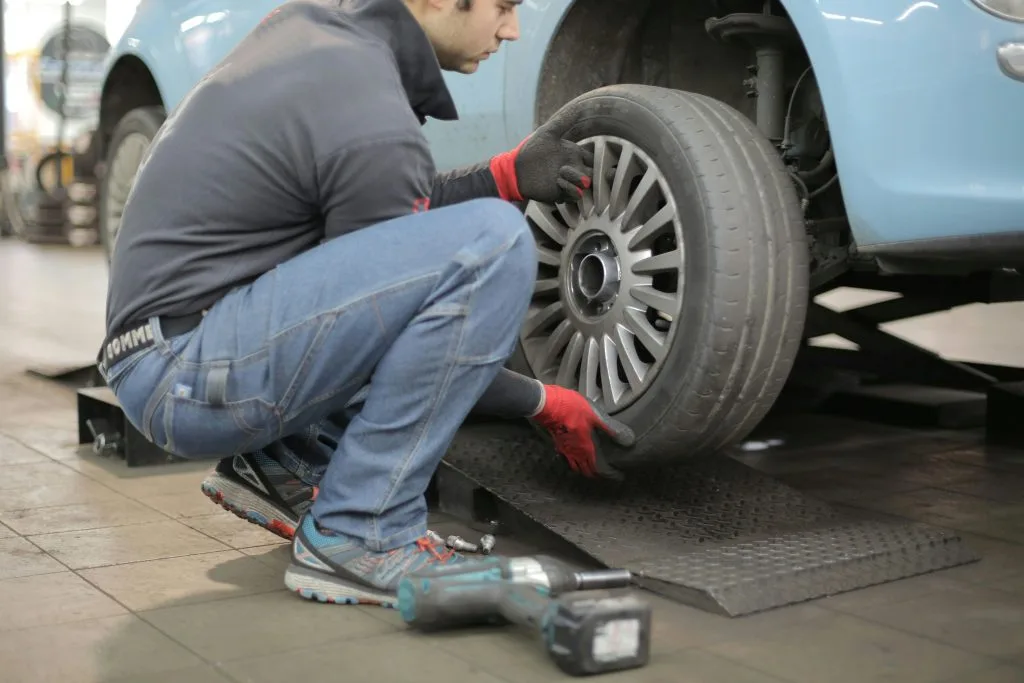 A mechanic kneels beside a lifted car, replacing its tire