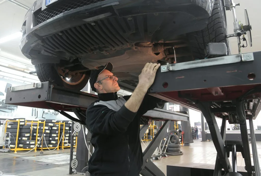 A mechanic inspects the underside of a raised vehicle in a garage