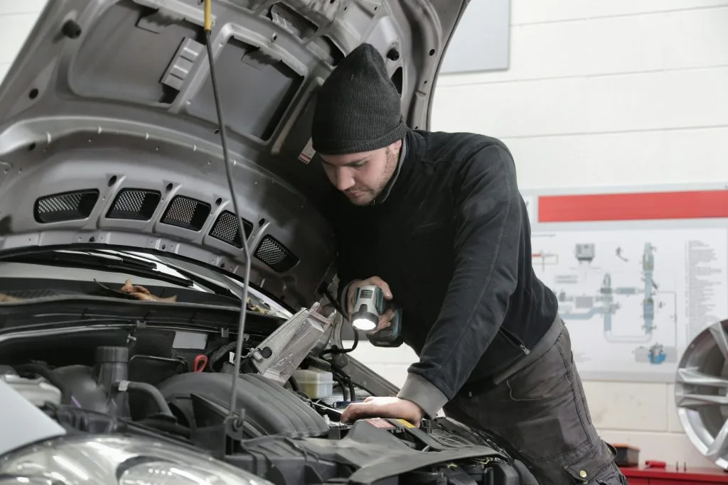 A mechanic inspects a car's engine while using a tool