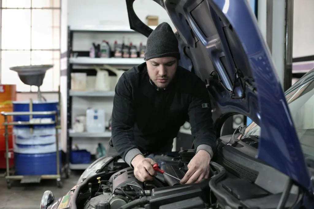 A mechanic in a hooded sweatshirt works on a car engine