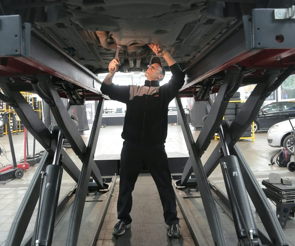 A mechanic works beneath a lifted vehicle, using tools to perform maintenance