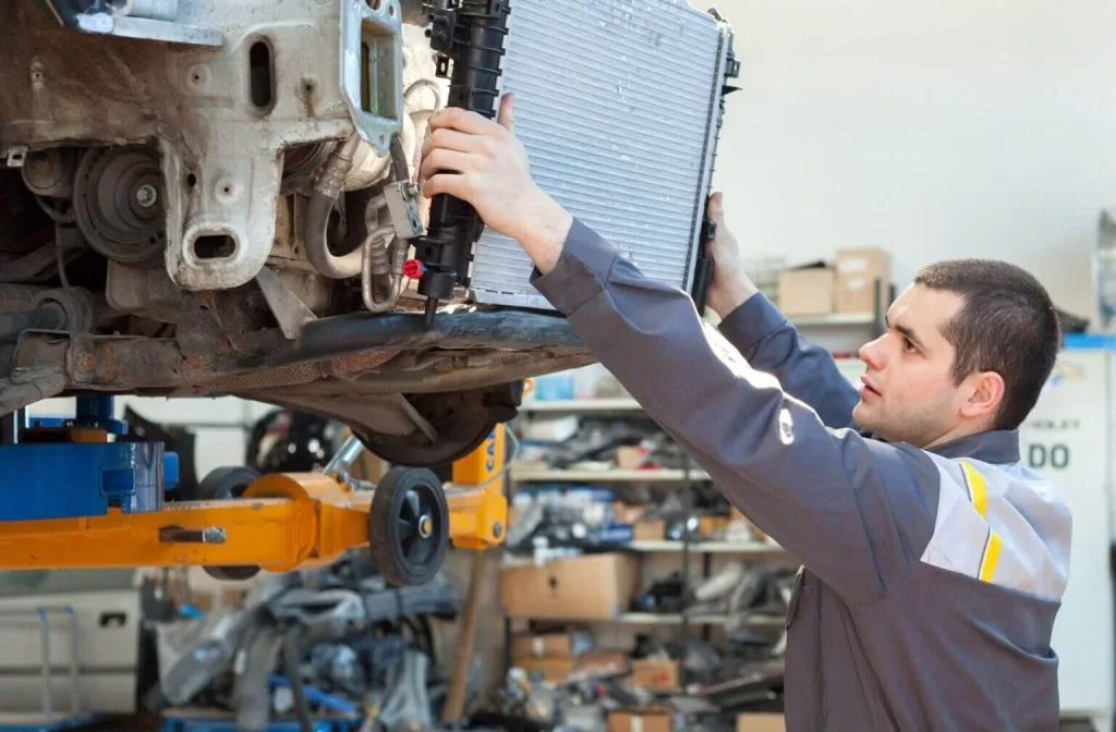 A mechanic installs a radiator under a lifted car in a workshop