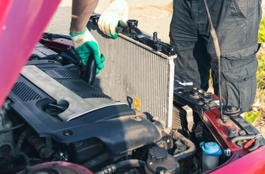 A person in gloves works on removing a radiator from a car engine