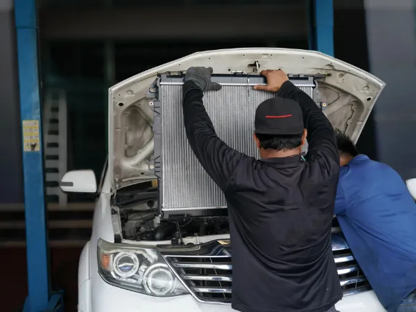 Mechanic replacing industrial radiators under the hood of a white vehicle