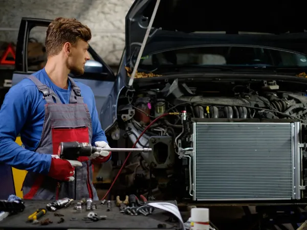 Mechanic performing radiator repair on a car engine with a power tool
