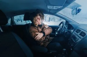 A person in a car, wearing a fur-lined coat, appears cold and uncomfortable