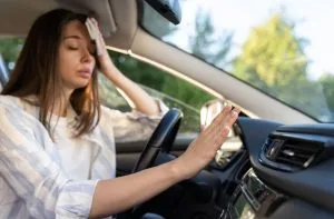 A woman appears stressed, holding her forehead while sitting in a parked car