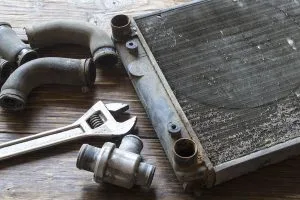 A disassembled radiator sits alongside worn hoses and a wrench on a wooden surface