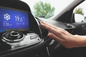 A hand reaches toward a car's climate control display showing a cold temperature setting