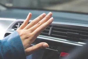 A hand is reaching towards a car's air vent, possibly adjusting the airflow