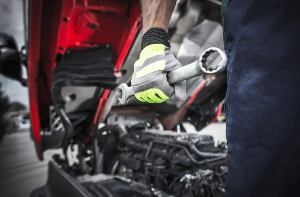 A mechanic grips a wrench while working on an engine beneath a vehicle