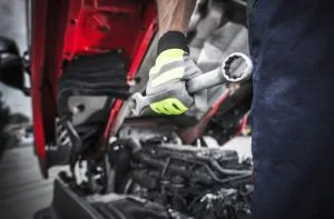 A mechanic grips a wrench while working on an engine beneath a vehicle
