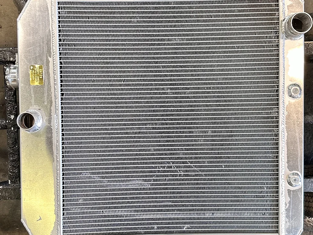 A metallic car radiator with multiple fins and fluid ports is showcased