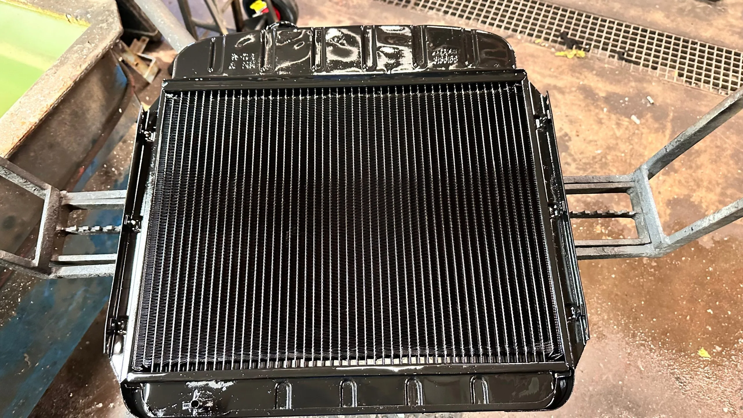 A freshly painted black radiator sits on a workbench, showcasing its horizontal fins
